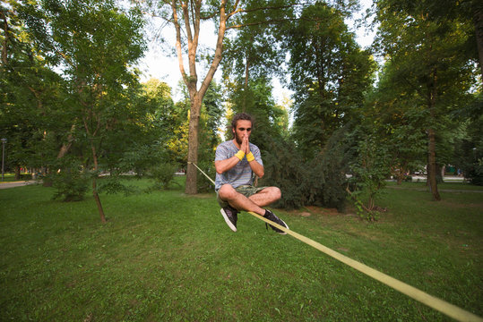 Young man sitting in lotus position on slackline