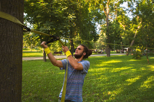 Young bearded man setting up a slackline in the park