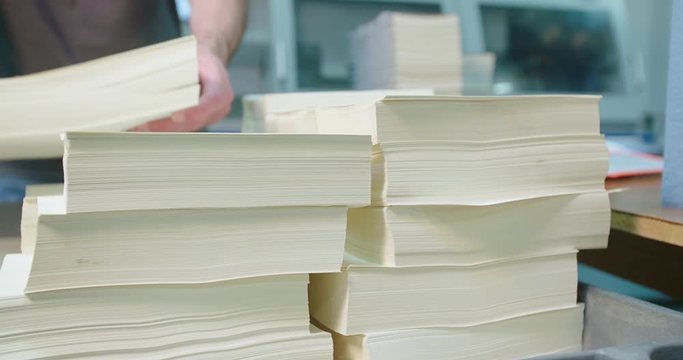 Worker Grabs Stack of Book Pages for Binding Machine. a view from right to left from a stack of book pages as a worker grabs a stack for the binding machine
