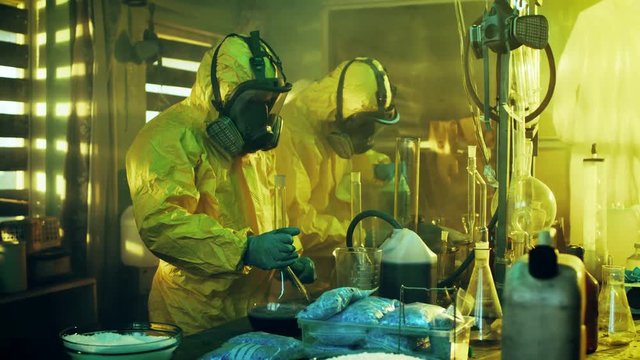 In the Underground Laboratory Two Clandestine Chemists Cook Drugs. They Wear Masks and Coveralls and Work with Beakers and Toxic Chemical Compounds.