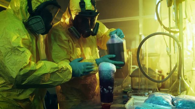In the Underground Drug Laboratory Two Clandestine Chemists Mix Chemicals while Cooking Narcotics. They Use Canisters and Beakers, Toxic Compounds Create Smoke. They Work in the Abandoned Building.
