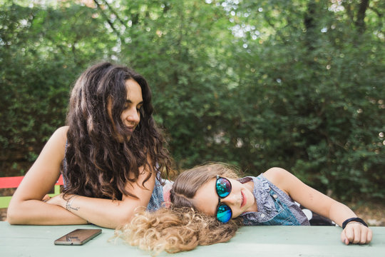 Tired 6 years old girl laying on the table wearing sunglasses next to her mother