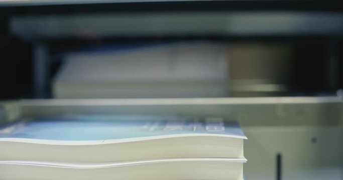 Automated Book Trimmer Machine Brings in Book for Cutting. a close up of a machine bringing in a soft cover book to be trimmed for production
