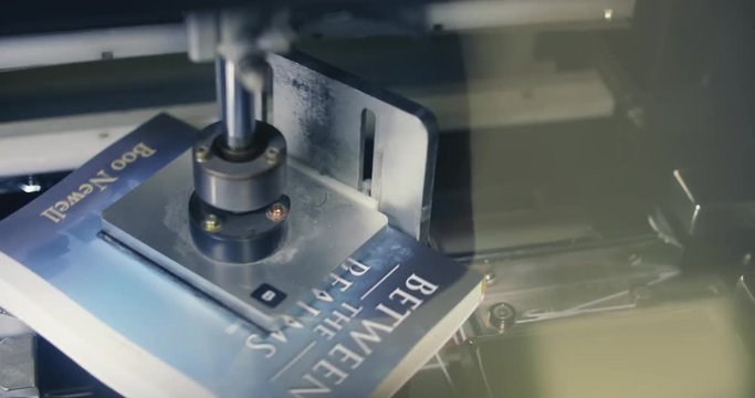 Automated Book Trimmer Machine Spins and Cuts Book Above. a close up above view of a machine spinning a paperback book to be trimmed on all sides
