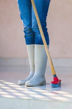 Feet in rubber boots of a woman washing the porch