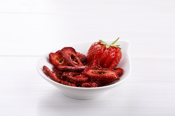 Fresh strawberry and dried strawberry slices on white wooden table.