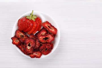 Fresh strawberry and dried strawberry slices on white wooden table.
