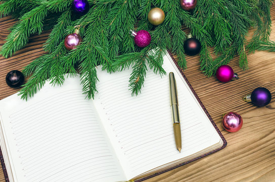 Open book with blank empty pages in Christmas tree branches with christmas balls around on burnt wooden board background. Text new year greetings.