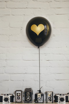 Black balloon decorated with golden heart and collection of old reflex cameras