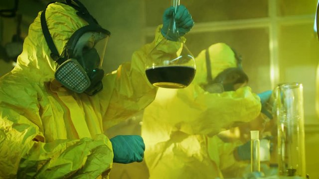 In the Underground Drug Laboratory Team of Clandestine Chemists Synthesises Illegal Drugs, One Holds Beaker with Chemicals and Checks it's Consistency. They Cook Drugs in the Abandoned Building.
