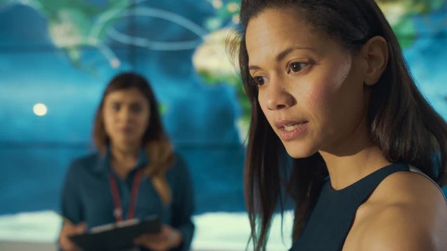 Businesswoman talking to colleagues in control room with large world map