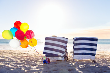 Two beach chairs and a bunch of balloons at the beach at sunset