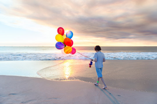 Boy with a bunch of colorful balloons, walking at the beach