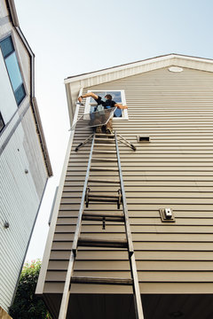Window Washer On Top Of Tall Ladder Cleaning Fourth Story Window