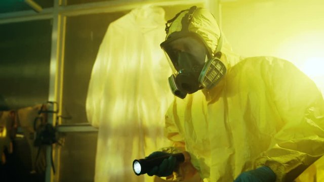 Two Officers from Hazardous Materials Police Unit Inspect Busted Drug Making Laboratory. They Wear Hazmat Suits and Gas Masks and Walk Carefully with Flashlights.