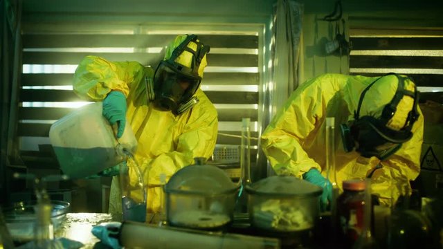 In the Underground Drug Laboratory Clandestine Chemists Wearing Protective Masks and Coveralls Mix Chemicals for Synthesising New Batch of Addictive Narcotics. They Work in the Abandoned Building.