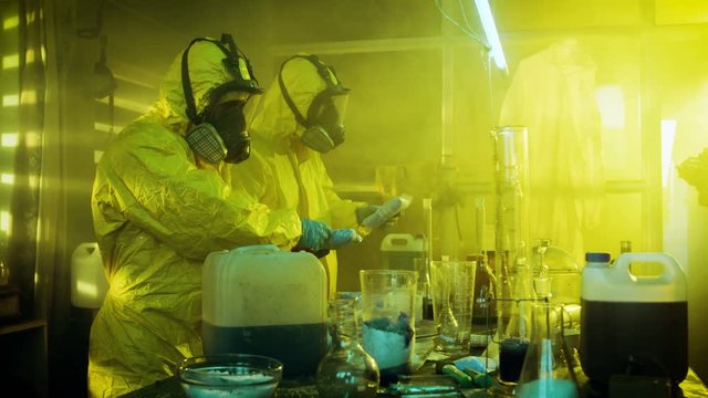 In the Underground Laboratory Two Clandestine Chemists Pack Bags of Drugs into Boxes. Laboratory is Full of Glassware and Other Narcotics Production Related Equipment. 