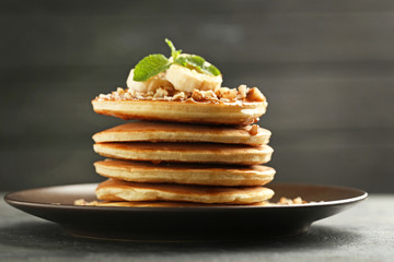 Tasty pancakes with walnuts and bananas on grey wooden plate