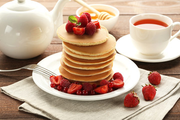 Tasty pancakes with berries and cup of tea on wooden table