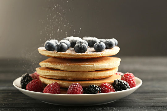 Tasty pancakes with berries on black wooden table