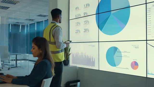  Business team looking at large video screen & computers with charts & data