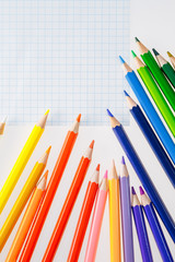 Color pencils on white background. Free space for text. Tools for drawing, education, school, creativity. Sheet of the notebook on the table.