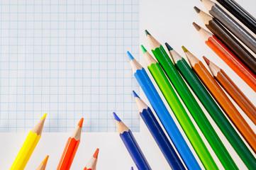 Color pencils on white background. Free space for text. Tools for drawing, education, school, creativity. Sheet of the notebook on the table.