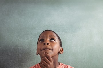 Thoughtful boy against green board in classroom