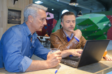 two men using a laptop in a cafe bar