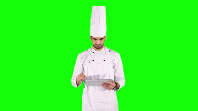 Male Caucasian chef using a digital tablet while standing in the studio and wearing uniform in front of green screen background