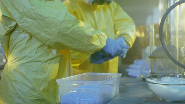 In the Underground Laboratory Clandestine Chemists in Protective Coveralls Pack Newly Cooked Batch of Drugs in the Bags for Further Street Distribution. 