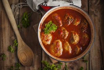 meat cutlets in tomato sauce, baked in a frying pan. Decorated with parsley. on a wooden background, in rustic style in brown colors. Meat lunch for the family