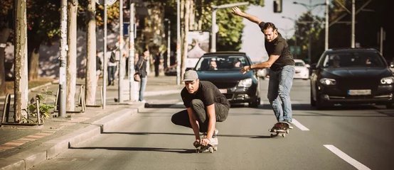 Afwasbaar fotobehang Two skateboarders riding skateboard slope on the city streets © guruXOX