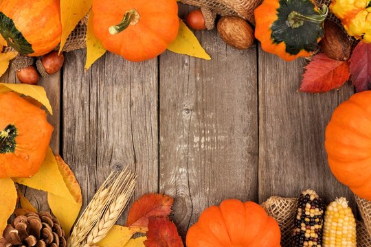 Autumn frame of colorful leaves and pumpkins over a rustic wood background