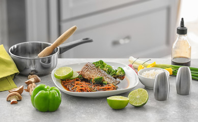 Plate with delicious fish in sauce and vegetables on table in kitchen