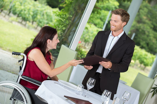 smiling male waiter serving disabled beautiful woman