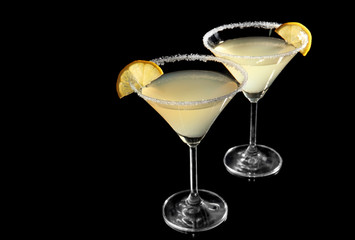 Glasses of lemon drop martini with slices of fruit on black background