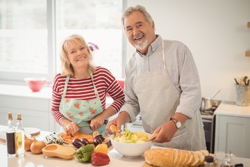Obraz na płótnie Canvas Smiling senior couple preparing salad in kitchen