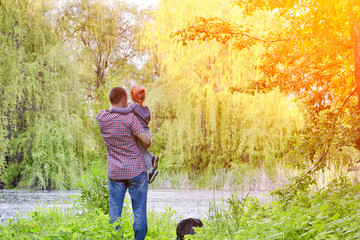 Dad with a little son are standing on the shore of a forest lake, rear view
