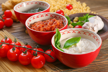 Delicious pesto, bolognese and white sauces for pasta in bowls on table