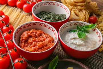 Delicious pesto, bolognese and white sauces for pasta in bowls on table
