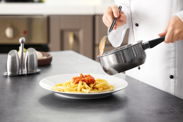 Female chef adding bolognese sauce to delicious pasta on plate