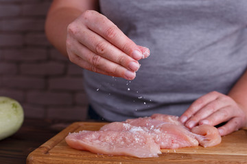 Overweight woman hands adding salt to raw chicken breasts. Dieting, healthy low calorie food, weight losing concept