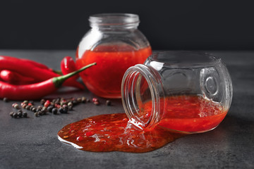 Overturned glass jar with spilled chili sauce on grey table