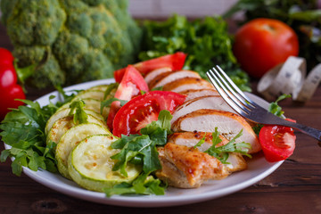 Diet concept, healthy lifestyle, low calorie food.  Baked chicken breasts with zucchini and salad, measuring tape and vegetables on the table