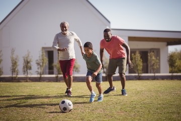 Boy playing football with his father and grandson