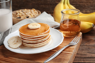 Plate with yummy banana pancakes on wooden table