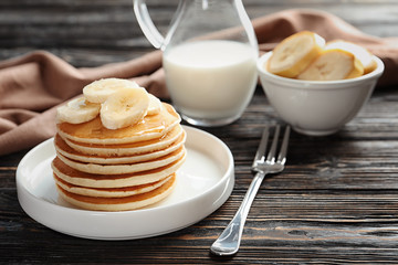 Plate with yummy banana pancakes on wooden table