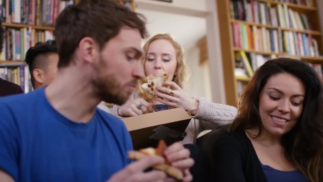 Large group of happy young friends eating takeaway pizza at home.