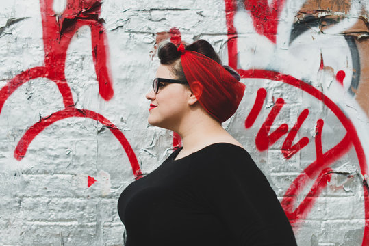Stylish woman in red scarf standing against graffiti wall